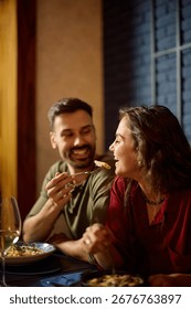 Happy couple having fun while eating in restaurant. Man is feeding his girlfriend. 