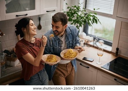 Happy couple having fun while eating pasta in the kitchen. 