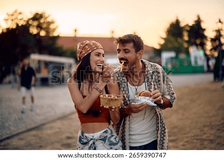 Happy couple having fun while sharing food during open air music festival in summer. 