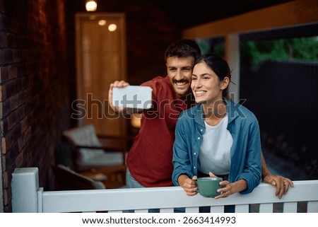 Happy couple having fun while taking selfie on the porch of their new home. Copy space. 