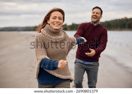 Happy couple having fun while holding hands and running in autumn day. Focus is on woman. 