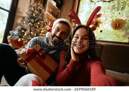 Happy couple having fun while taking selfie on Christmas day at home and looking at camera.