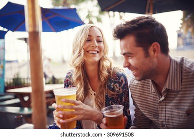 Happy Couple Having A Good Time Drinking Beer Together At Outdoor Pub Or Bar