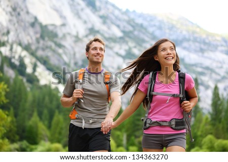 Happy couple of hikers hiking holding hands joyful, cheerful and fresh. Young active multiracial couple in outdoor activity hike in Yosemite National Park, California, USA. Asian woman, Caucasian man.