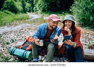 Happy couple of hikers using cell phone while relaxing in the forest. - Powered by Shutterstock