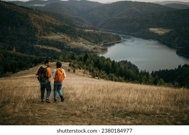 Happy couple hiking with backpacks on a hill, enjoying the view of a distant lake - Powered by Shutterstock