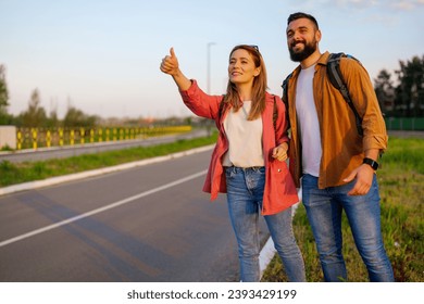 Happy couple hitchhiking on roadside trying to stop car.