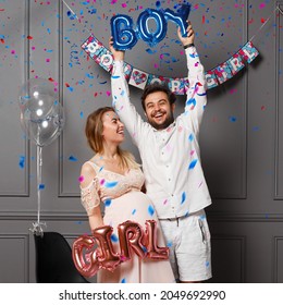 Happy couple holding balloons with inscription boy or girl during gender reveals party, over confetti and balloons. - Shutterstock ID 2049692990
