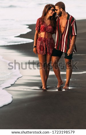 Happy couple holding hands walking on the sandy beach. Couple in love at sunset by the sea. Couple in love on vacation. Honeymoon trip. Romantic couple enjoying a beach walk at sunset 