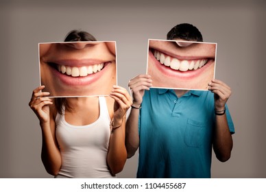pareja feliz sosteniendo una foto de una boca sonriendo en un fondo gris