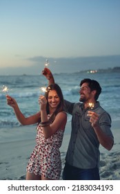 happy couple holding sparklers celebrating new years eve on beach at sunset with sparkle firework