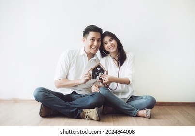 Happy Couple Holding Wooden House Model With Stethoscope.  Concept Of House Inspection.