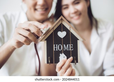 Happy Couple Holding Wooden House Model With Stethoscope.  Concept Of House Inspection.