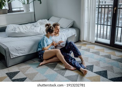 Happy couple at home, man and woman surfing the Internet, happy couple making a video call from home, young couple with a laptop, spending time together at home, young couple in pyjamas with a laptop