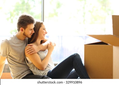 Happy couple hugging moving new house sitting on the floor and looking through the window
