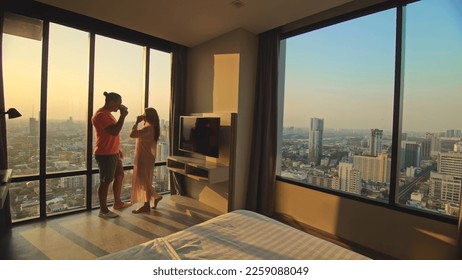 Happy couple husband and wife looking on beautiful sun light together at home, enjoying hug and morning coffee near big window. Young adult couple kissing and hugging in kiss, enjoying love embracing - Powered by Shutterstock