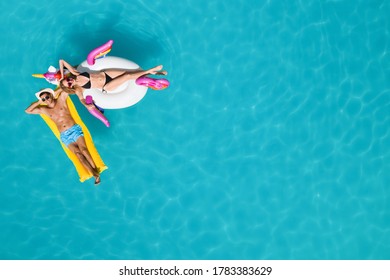 Happy couple with inflatable ring and mattress in swimming pool, top view. Summer vacation - Powered by Shutterstock