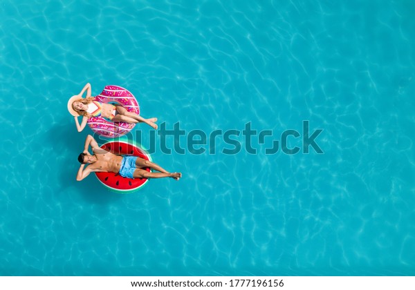 Happy couple with inflatable\
rings in swimming pool, top view and space for text. Summer\
vacation
