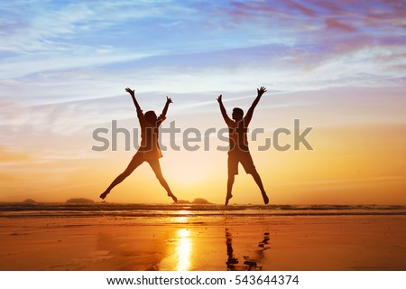 happy couple jumping on the beach at sunset, family summer holidays or honeymoon
