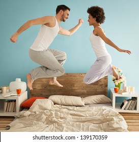 Happy couple jumping together on their bed.