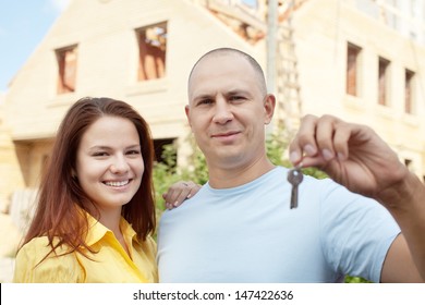 Happy couple with key against building new brick house   