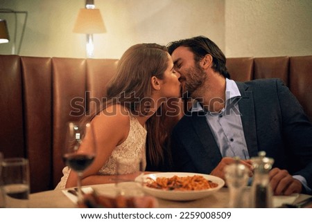 Happy couple, kiss and love for dinner date, embrace or relationship affection at night in restaurant. Man kissing woman lips in romance for fine dining, celebration or anniversary on valentines day