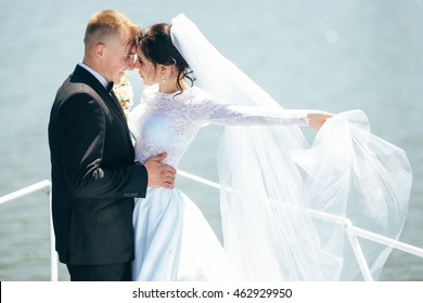 A happy couple kissing at the bow of a sail boat on a calm blue sea. Groom kissing bride on a sailboat. Wedding ceremony, Love story.