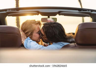Happy couple kissing in convertible car - Romantic people having tender moment during road trip in tropical city - Love relationship and youth vacation lifestyle concept