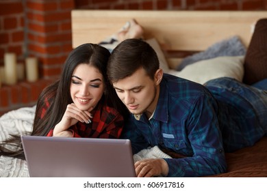 Happy couple with laptop shopping online at home, browsing internet in bed, smiling and having fun