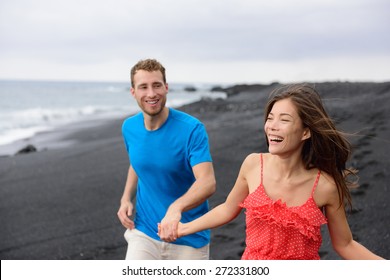 Happy Couple Laughing Together Walking On Beach Holidays. Vacation Concept Of Two Adult People Holding Hands On Secluded Black Sand Beach On Volcanic Island Enjoying Their Getaway Holiday.