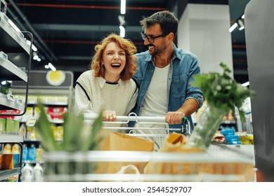 Happy couple laughs while shopping for groceries in a supermarket, enjoying each other's company among fresh produce, dairy, and meat - Powered by Shutterstock