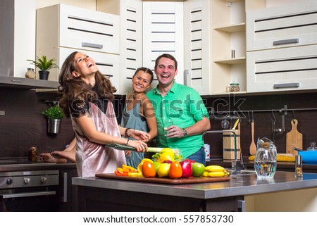 Happy couple looking to cooking woman in kitchen