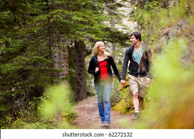 A happy couple looking at eachother and walking in the forest holding hands