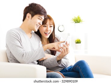 Happy  Couple Looking At Smart Phone In Living Room