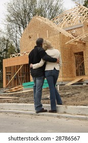 Happy Couple Looking At Their New Home Still Under Construction.