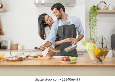 Happy couple in love cooking in the kitchen counter at home and hugging - Powered by Shutterstock