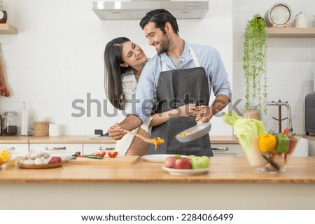 Happy couple in love cooking in the kitchen counter at home and hugging