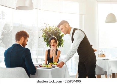 Happy Couple In Love Having Romantic Dinner In Luxury Gourmet Restaurant. Waiter Serving Meal. People Celebrating Anniversary Or Valentine's Day. Romance, Relationship Concept. Healthy Food Eating.