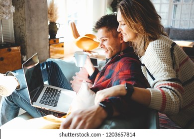 Happy couple in love at home. Man and woman sitting on the couch and watching TV series on laptop. Bright loft apartment