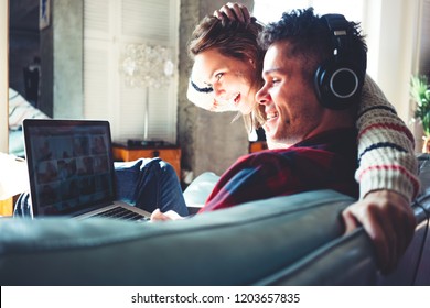 Happy couple in love at home. Man and woman sitting on the couch and watching TV series on laptop and listening music. Bright loft apartment