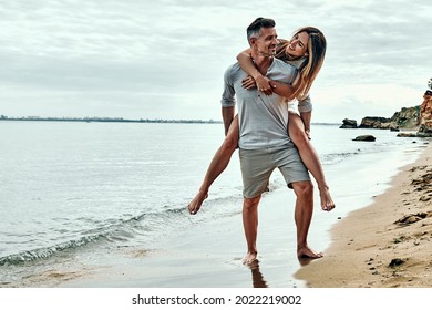 Happy Couple In Love On Beach Summer Vacations. Joyful Woman Piggybacking On Husband Having Fun. Full Length. Copy Space.