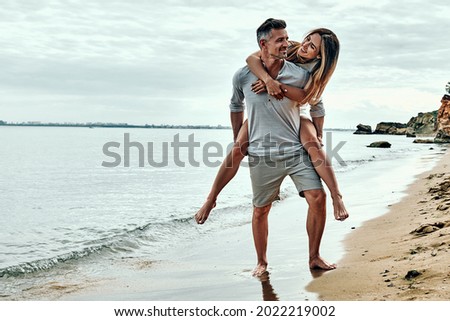 Happy couple in love on beach summer vacations. Joyful woman piggybacking on husband having fun. Full length. Copy space.