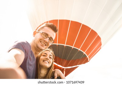 Happy Couple In Love On Honeymoon Vacation Taking Selfie At Hot Air Balloon - Summer Travel Concept With Young People Travelers Having Fun At Excursion - Vintage Contrast Retro Filter With Backlight