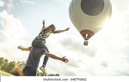Happy couple in love on honeymoon vacation cheering at hot air balloon - Summer travel concept with young people travelers having fun at trip excursion - Vintage contrast retro filter with backlight