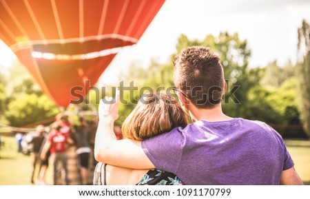 Happy couple in love on honeymoon excursion waiting for hot air balloon ride - Summer travel concept with young people travelers having fun at trip vacation - Bright warm filter with backlight