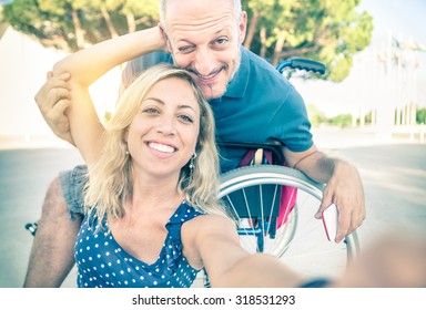 Happy couple in love taking selfie in urban city background - Disability positive concept with man on wheelchair - Vintage filtered look with soft focus on smiling woman due to sun flare halo - Powered by Shutterstock