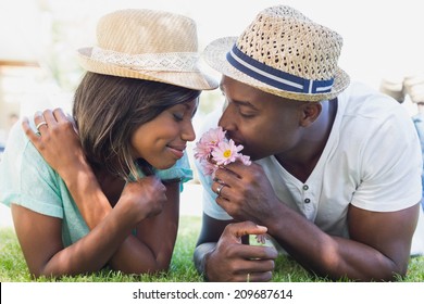 Happy Couple Lying In Garden Together Smelling Flowers On A Sunny Day