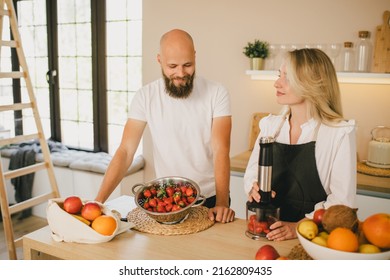 Happy Couple Making Smoothies Using Blender And Fresh Fruits On The Kitchen. Healthy Food.