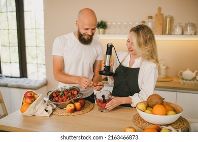 Happy Couple Making Smoothies Using Blender And Fresh Fruits On The Kitchen. Healthy Food.