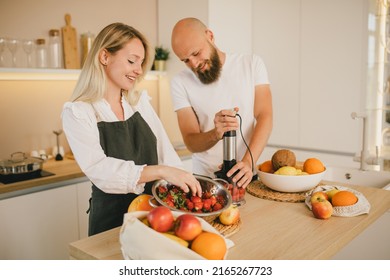 Happy Couple Making Smoothies Using Blender And Fresh Fruits On The Kitchen. Healthy Food.